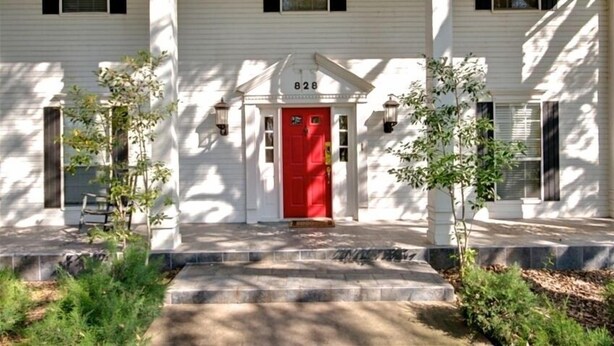 A white house with a red door and black shutters, number 828, with a front porch and two small trees. - Granbury's  Luxurious  'Abbey Manor'. Walk to Historic Square (Granbury)
