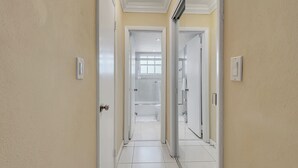 Un couloir menant à une salle de bain équipée d’une douche, de toilettes et d’un lavabo.