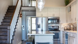A modern kitchen with stainless steel appliances, a central island, and a staircase with wooden steps. - Fantastic Ocean View Steps to Kamaole Beach 3 (Kihei)