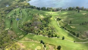 Eine Vogelperspektive auf einen Golfplatz mit mehreren Bahnen, umgeben von dichten Wäldern und einem Gewässer.