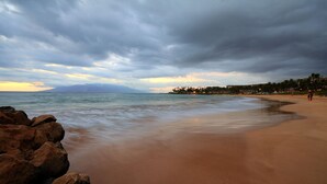 Uma praia com pedras em primeiro plano e mar calmo.