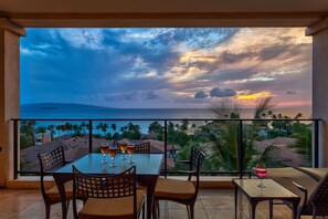 A balcony with a table and chairs, overlooking a sunset view with palm trees and a distant island. - Panoramic Ocean Views! -  Luxury Villa!  - Owner Direct! (Wailea-Makena)