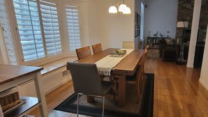 Et spiseområde med et træbord, stole og et tæppe. Et køkkenområde med en komfur og skabe er synligt.