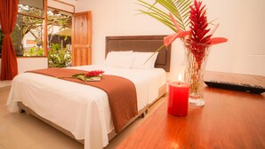 Una cama bien hecha con una colcha blanca y marrón, una vela roja y un florero con flores sobre una mesa de madera.