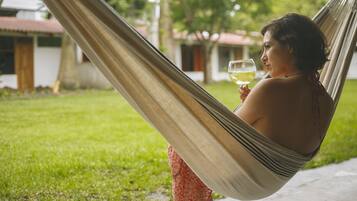 A person relaxing in a hammock outdoors, holding a glass of drink.