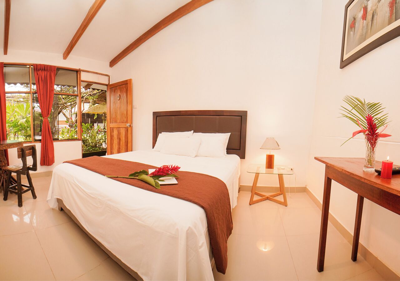 Habitación de hotel con cama, escritorio, silla, mesa y ventana con cortinas.