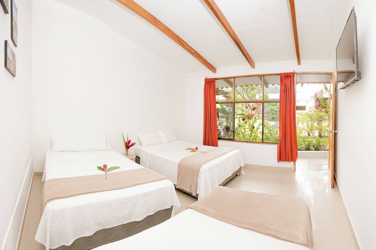 Une chambre d’hôtel avec deux lits, une grande fenêtre avec des rideaux, un téléviseur à écran plat et une vue sur la verdure environnante.