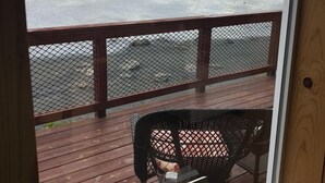 Una terraza de madera con barandal de metal, una silla y un cuadro en el alféizar de una ventana.