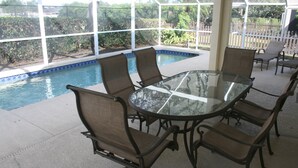 A covered patio with a glass table and six chairs, overlooking a swimming pool. - Beautiful Vacation Home 'Dolphin Wave'-Private Pool & Large Patio (Bradenton)