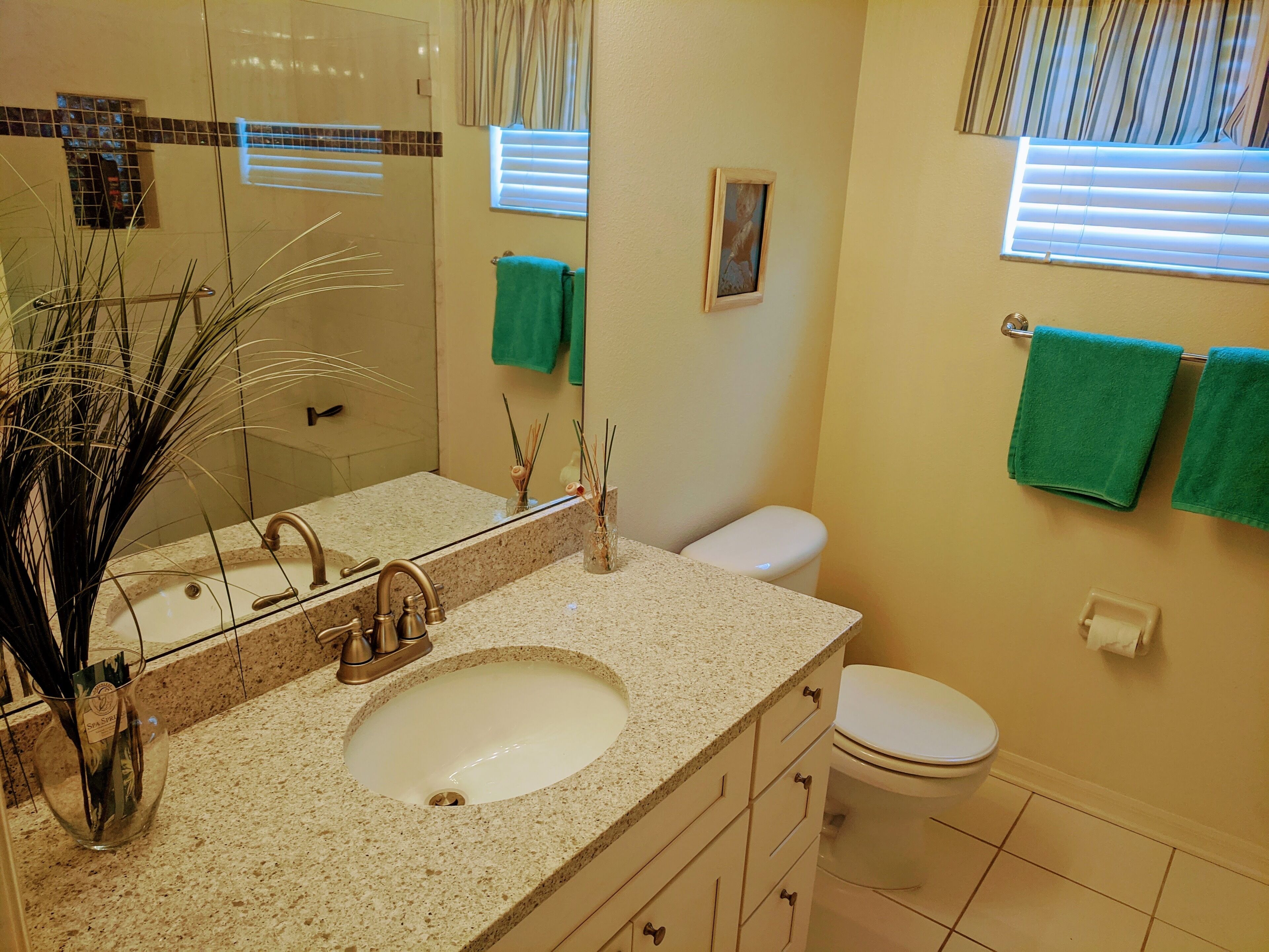 A bathroom with a sink, mirror, toilet, and window with blinds.