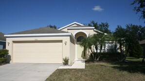 A single-story house with a beige garage door, a small front yard, and a palm tree. - Beautiful Vacation Home 'Dolphin Wave'-Private Pool & Large Patio (Bradenton)