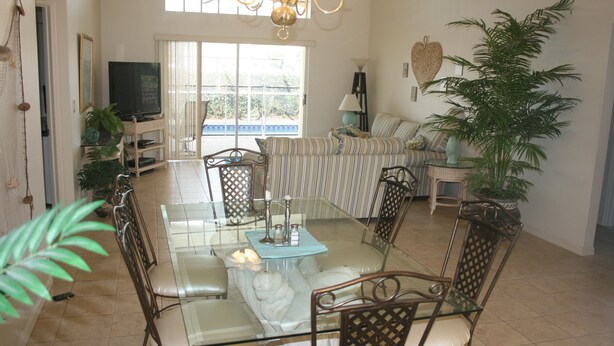 A spacious living room with a glass dining table surrounded by chairs, a sofa set, and a television. - Beautiful Vacation Home 'Dolphin Wave'-Private Pool & Large Patio (Bradenton)
