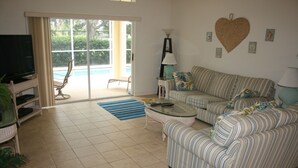A living room with a sofa, a television, and a table. There is a sliding glass door leading to a balcony. - Beautiful Vacation Home 'Dolphin Wave'-Private Pool & Large Patio (Bradenton)