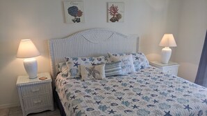A bedroom with a bed featuring a nautical-themed quilt, two bedside tables with lamps, and wall art depicting marine life. - Beautiful Vacation Home 'Dolphin Wave'-Private Pool & Large Patio (Bradenton)