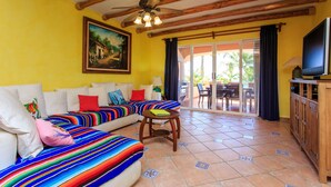 A bright living room with a wooden ceiling, a sofa with colorful cushions, a small table, and a television on a wooden cabinet. - Listen to the ocean at night! (puerta aventuras)
