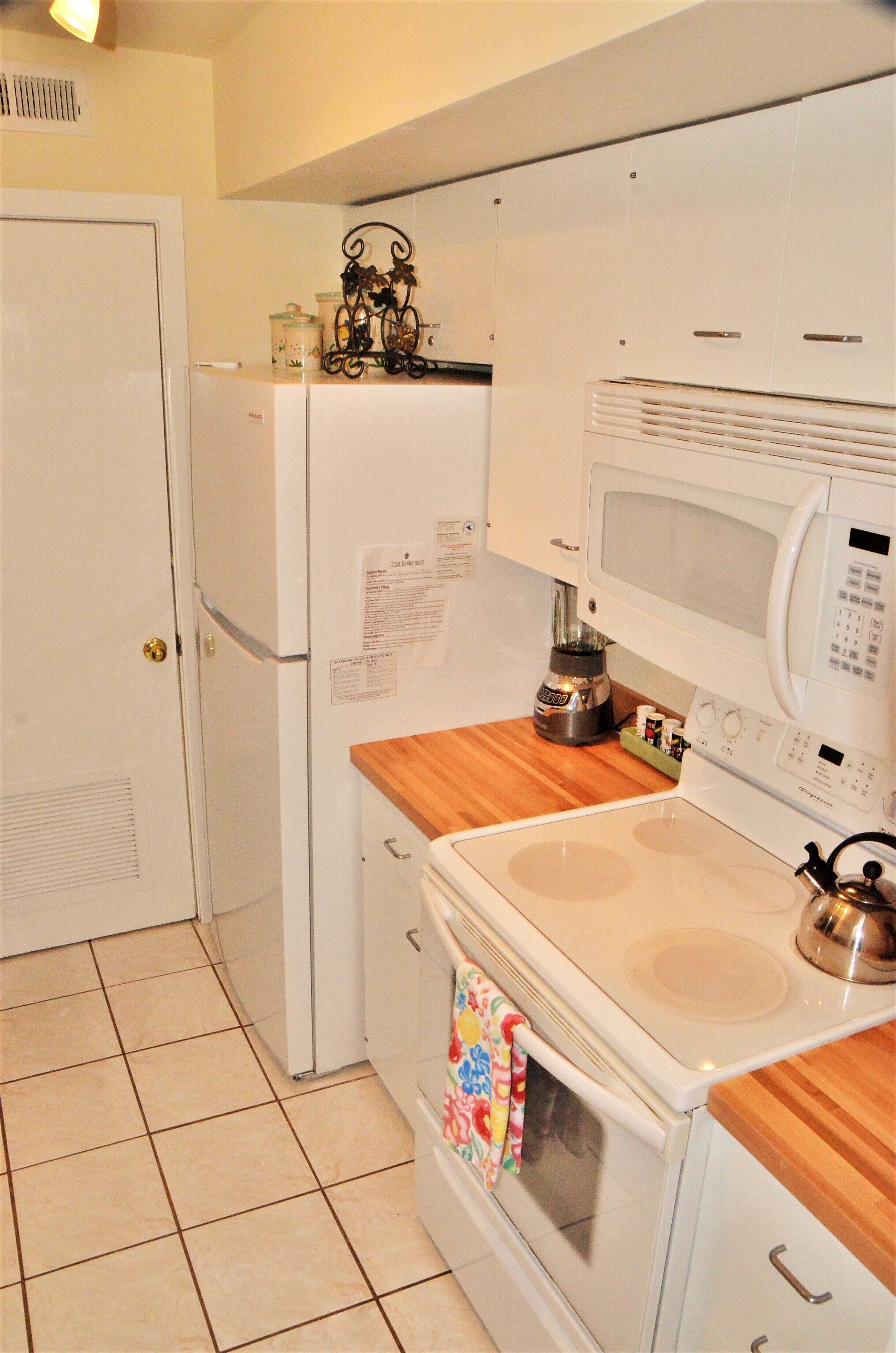 A compact kitchen with a refrigerator, microwave, stove, and wooden countertop.