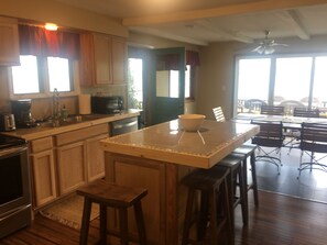 A kitchen with wooden cabinets, a central island with stools, a dining area with a table and chairs, and a view through the window. - Great Cayuga Lake House Complex for families, reunions, or just relaxing! (Trumansburg)