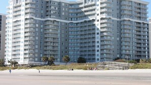 Un immeuble résidentiel à plusieurs étages, doté de balcons, situé près d’une plage.