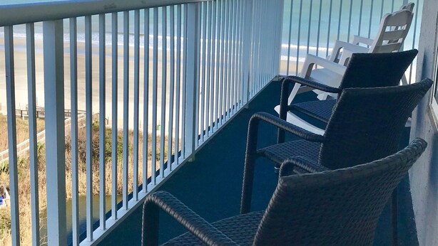 Un balcon avec des fauteuils en osier donnant sur une plage.