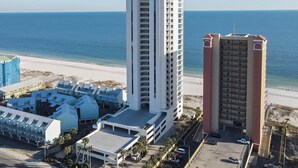 Un hotel frente al mar con un edificio alto de color blanco y otro más bajo de color rojo, ambos con balcones.