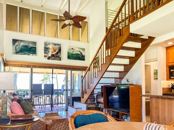 A spacious living area with a wooden staircase, a large TV, and a ceiling fan.