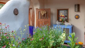 A rustic building with a wooden door, a blue cabinet, and various flowers in the foreground.