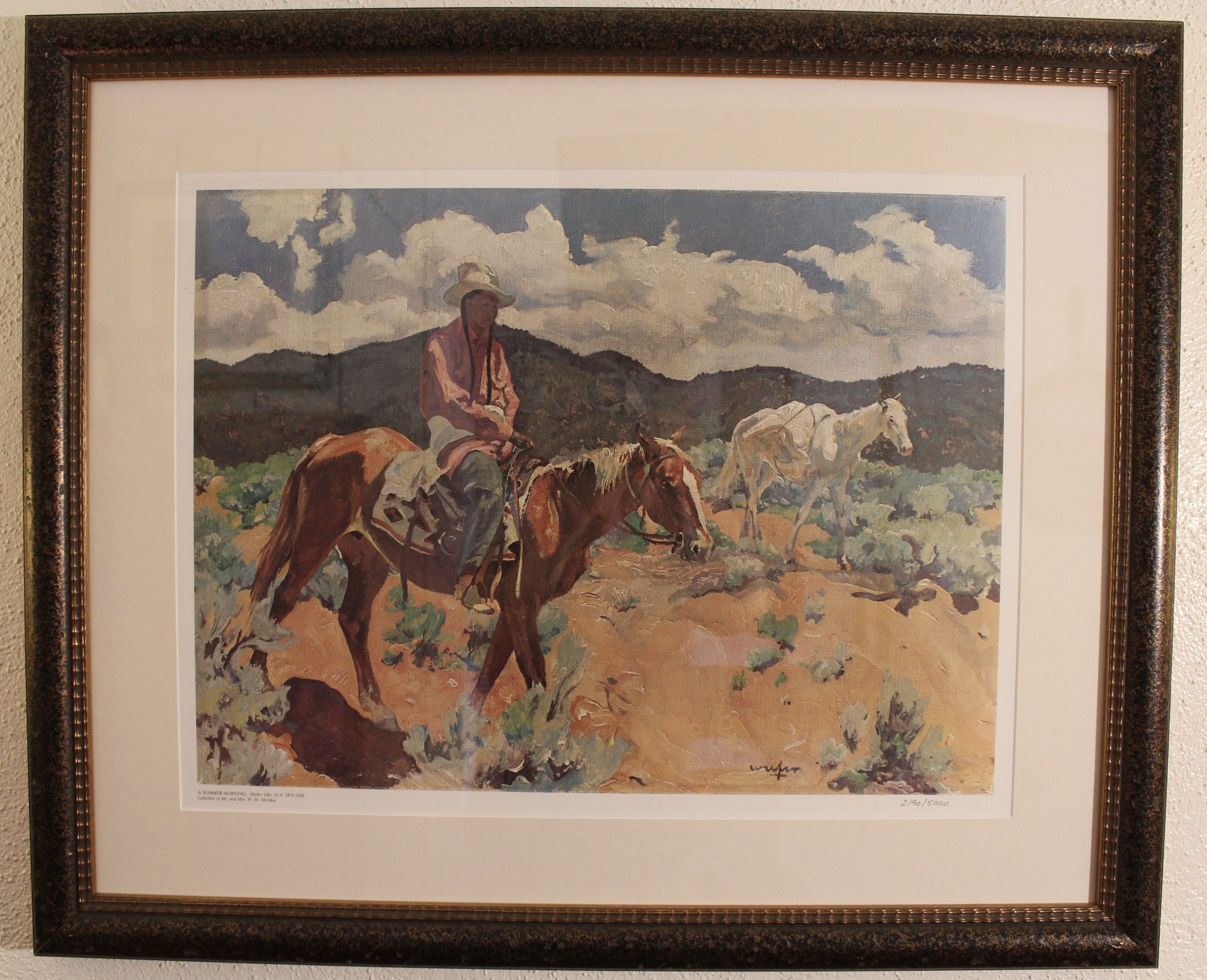 A framed painting of a cowboy on horseback with two horses, set against a landscape with mountains and clouds.
