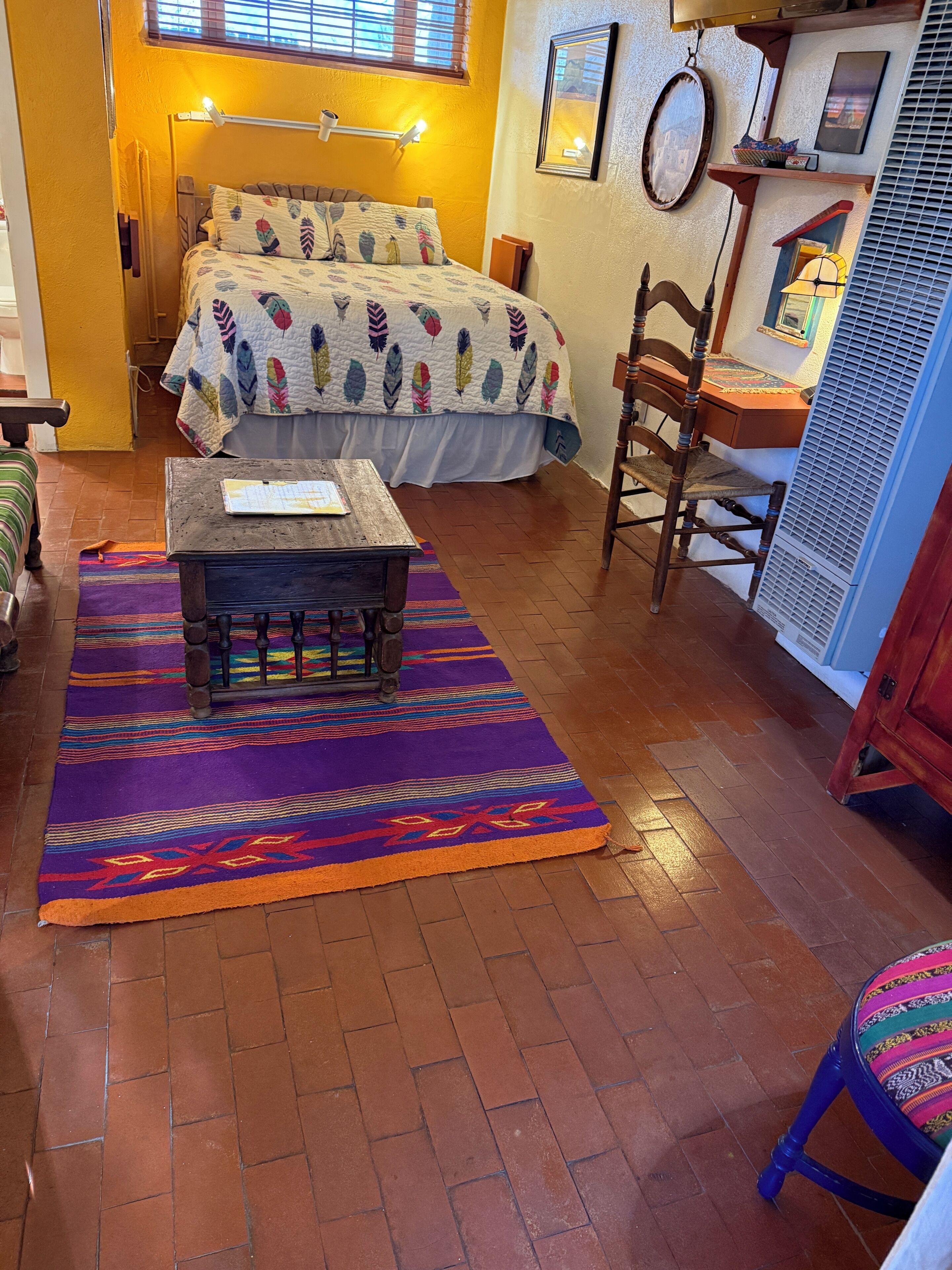 A cozy room with a bed, a wooden table, a chair, and a colorful rug.