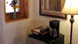 A small kitchenette with a refrigerator, a coffee maker, and a window with a wooden frame.