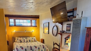 A cozy bedroom with a bed, a desk, a chair, a television, and a heater.