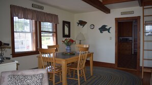 A dining area with a table and chairs, a lamp, a vase with flowers, and a fish-themed wall decoration. - Maine Midcoast Vacation at Lincolnville Beach (Lincolnville)