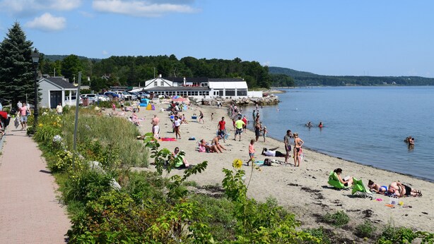 A beach with people sunbathing and swimming, a building with a white roof, and a clear sky. - Maine Midcoast Vacation at Lincolnville Beach (Lincolnville)