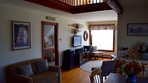 A living room with a wooden staircase, a television, a dining table with chairs, and a vase of flowers. - Maine Midcoast Vacation at Lincolnville Beach (Lincolnville)