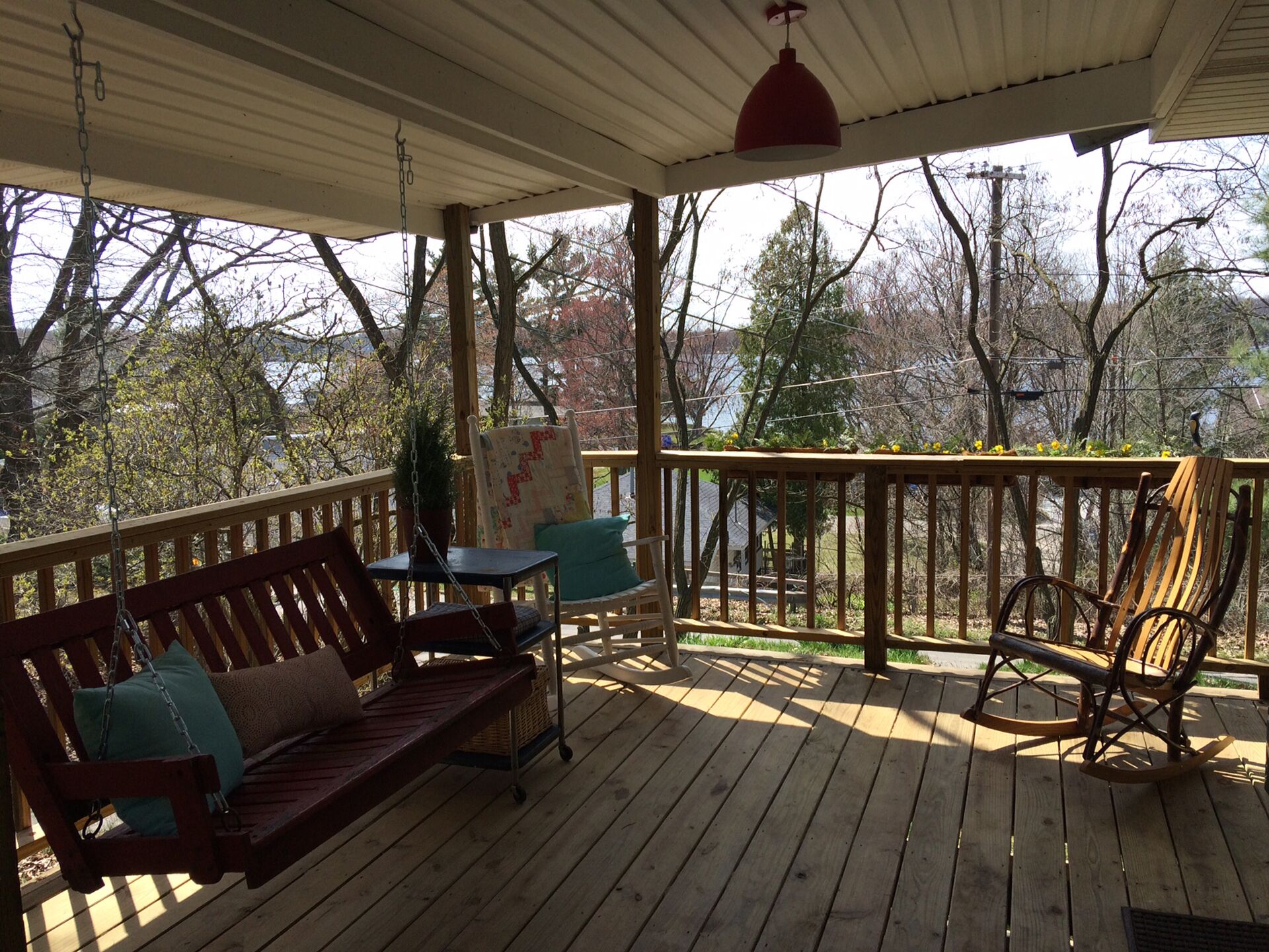 A wooden deck with a swing chair, a bench, and a rocking chair.