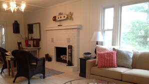 A living room with a fireplace, a sofa, a glass coffee table, and a dining area with chairs and a table.