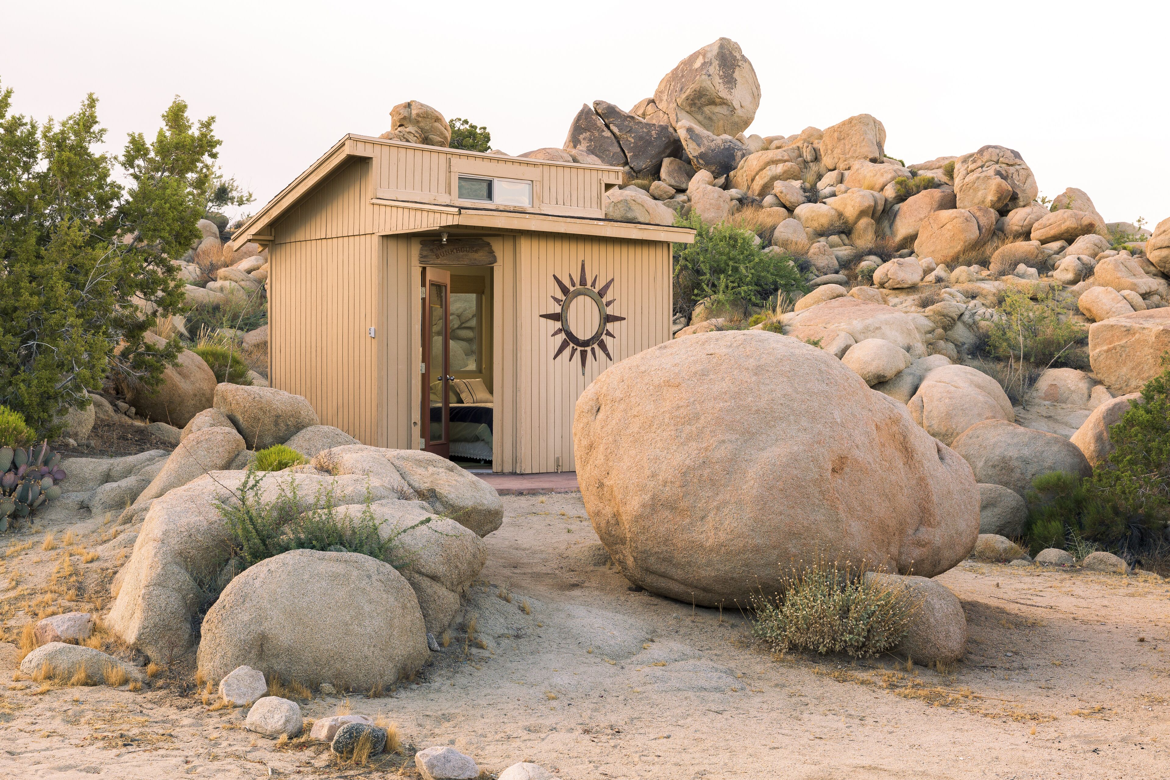 A small, single-story building with a sun symbol on the front, surrounded by large rocks and sparse vegetation.