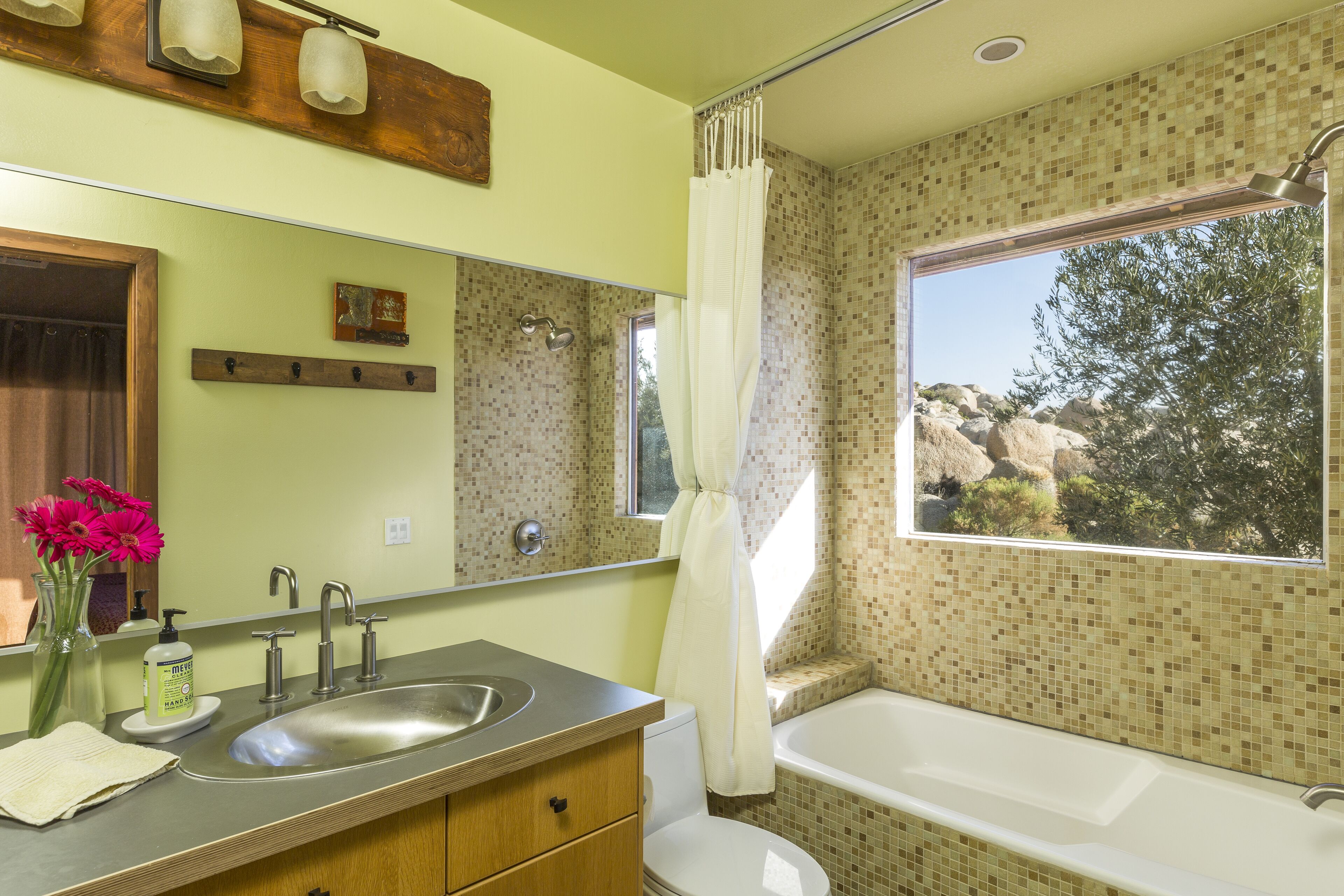 A bathroom with a large window, a sink, a bathtub, and a mirror.