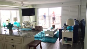 A spacious living room with a large TV, a sofa, a coffee table, and a balcony with a view. - Ocean Front 1st Floor walkout to 25'x50' deck on the Boardwalk/Beach at 4th St (Ocean City)