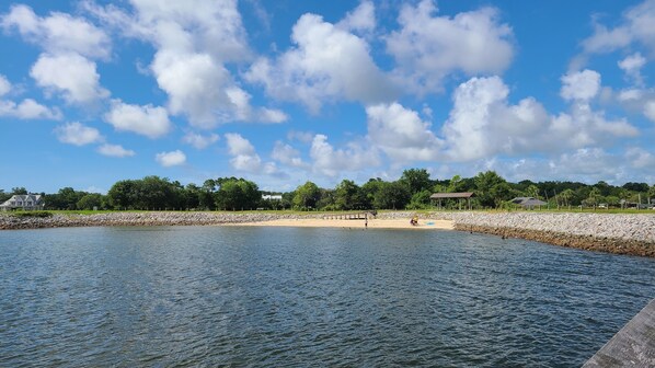 Une plage bordée d’une côte rocheuse, avec une jetée en bois et un kiosque.