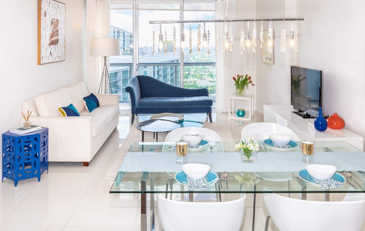 Un salon moderne avec une table à manger en verre, des canapés blancs et un canapé bleu.