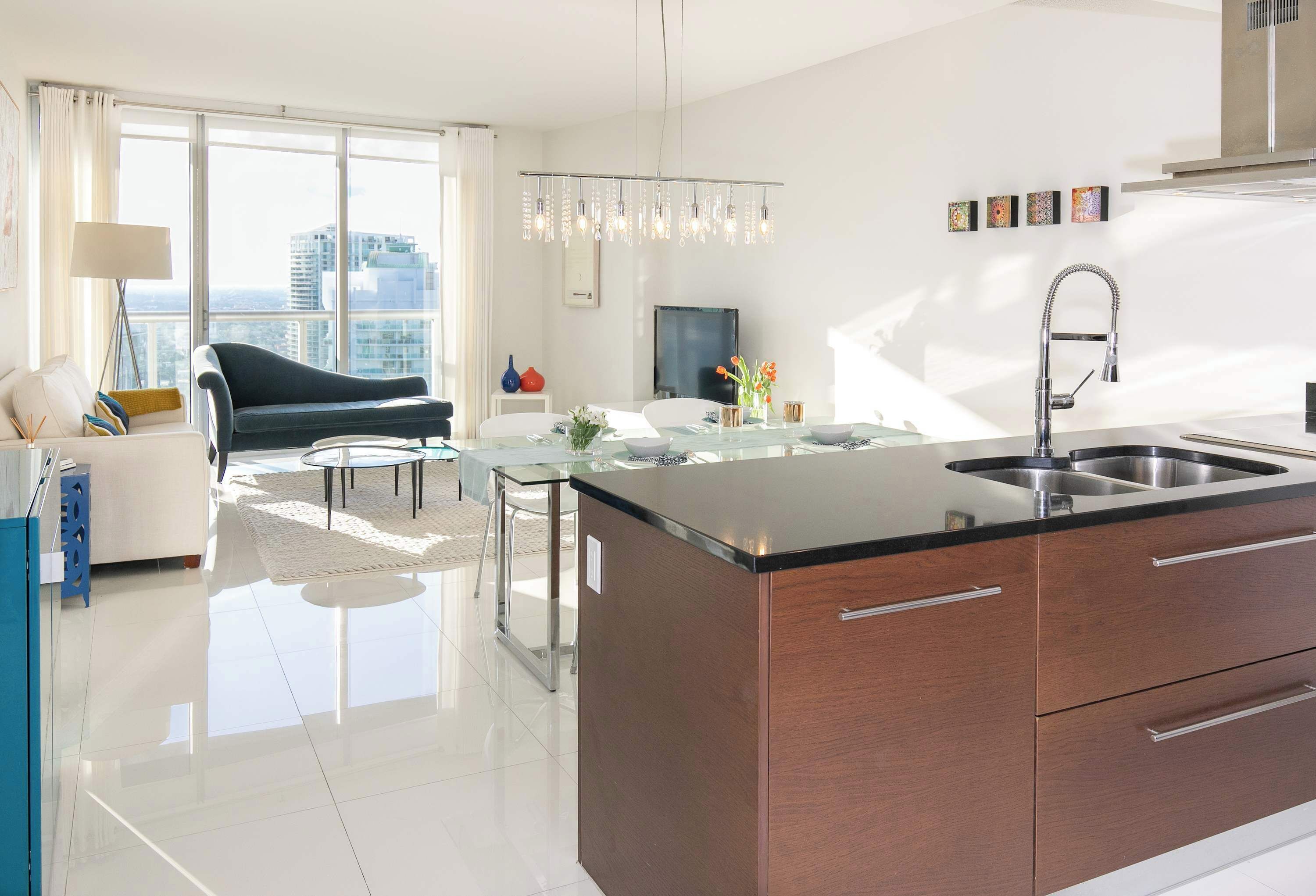 Une cuisine moderne dotée d’un îlot central, un coin repas avec une table en verre et un espace de vie comprenant un canapé et un fauteuil.