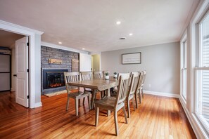 A dining area with a fireplace, wooden flooring, and a view of the outdoors.