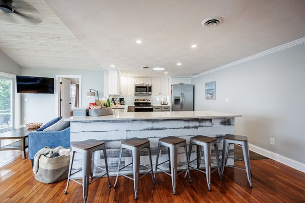 A modern kitchen with a central island, bar stools, and a dining area with a sofa and coffee table.