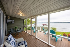 Una terraza techada con vista a un lago, muebles de exterior y un televisor de pantalla plana montado en la pared.