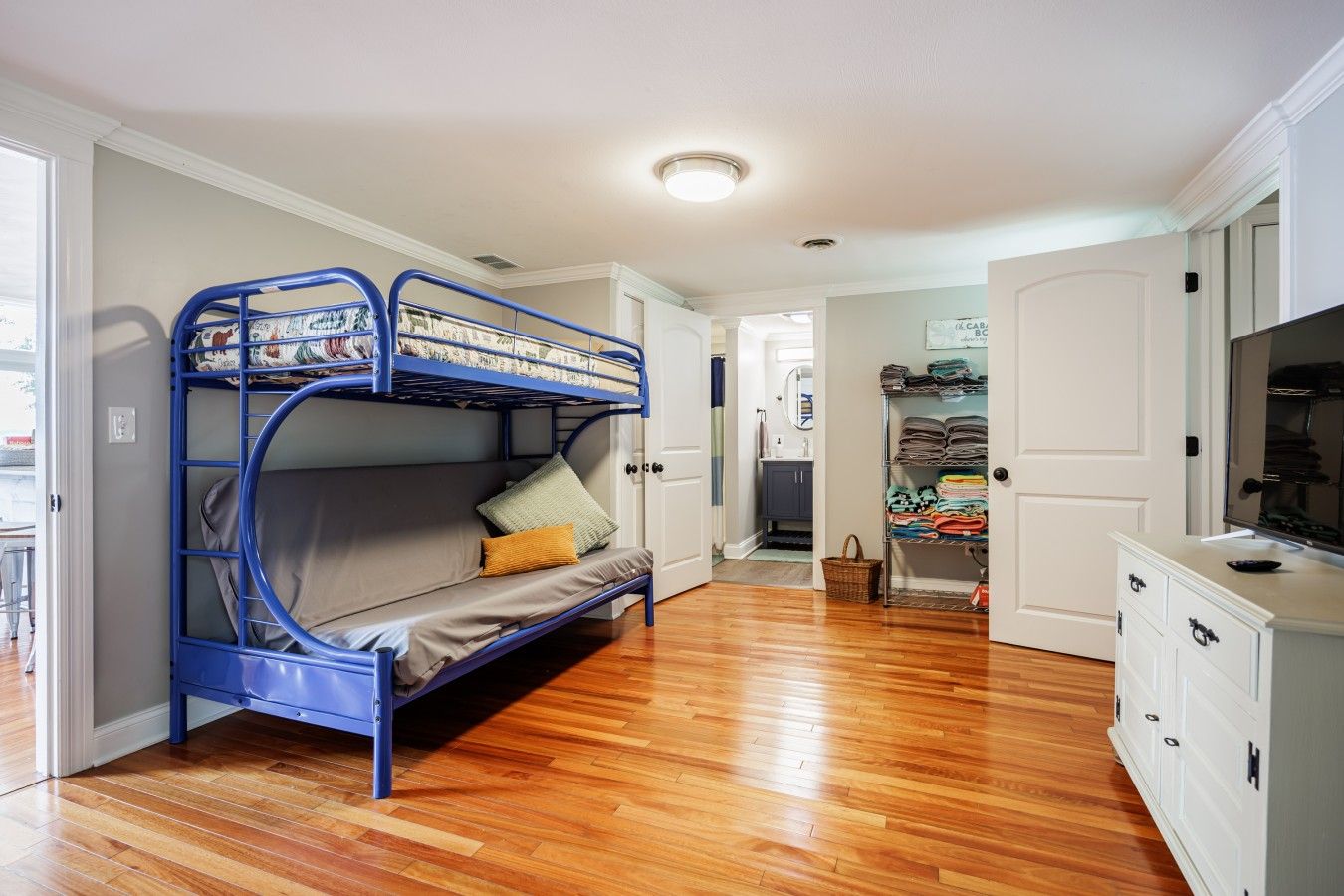 Quarto com beliche, televisão, guarda-roupa e banheiro ao fundo.