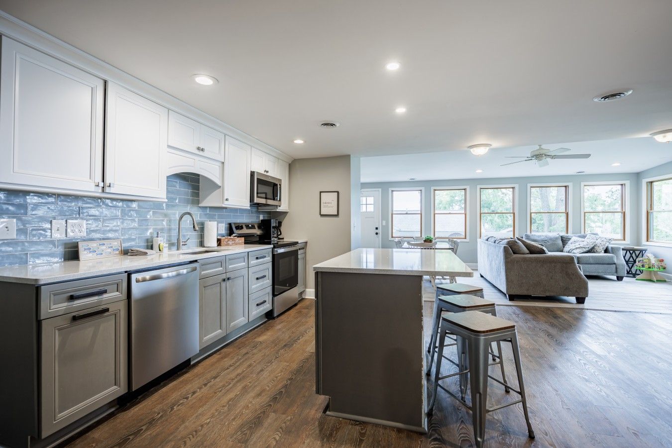 A modern kitchen with a central island, stainless steel appliances, and a dining area with a gray sofa and bar stools.