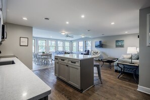 A modern kitchen with a central island, dining area with chairs, and a seating area with a sofa and a table.
