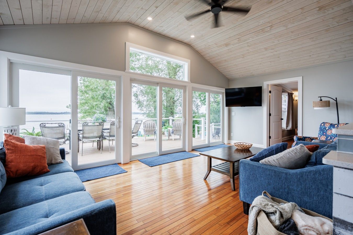 A spacious living room with a wooden floor, a blue sofa, a television, and a view of the outdoors through large sliding glass doors.