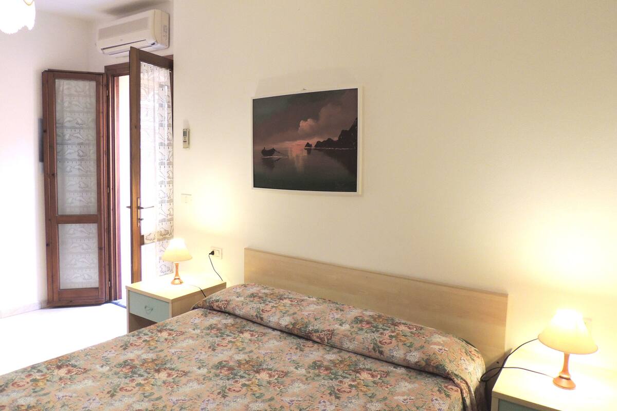 Ein Schlafzimmer mit einem Bett, zwei Nachttischen, einer Wandaircondition und einem gerahmten Bild an der Wand.