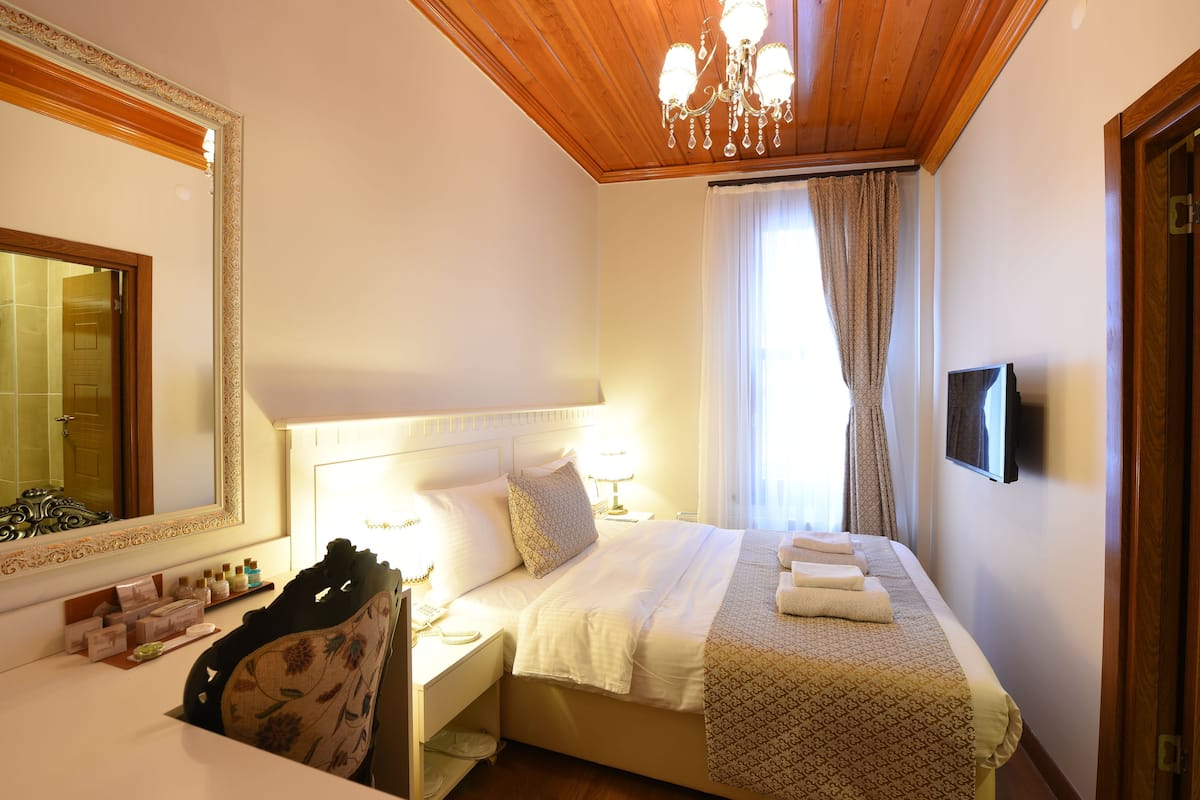 Une chambre d’hôtel avec un grand lit, une table de chevet avec une lampe, un miroir et un téléviseur fixé au mur.